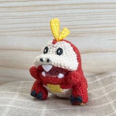 a crocheted red and white stuffed animal sitting on top of a wooden table