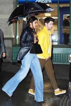 two people walking down the street with an umbrella over their heads and one person carrying a purse