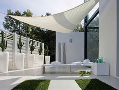 an outdoor area with white furniture and green grass in the foreground, under a shade sail