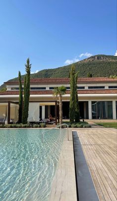 an empty swimming pool in front of a large house with mountains in the back ground