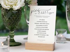 a table setting with white flowers and place cards on top of the menu card holder