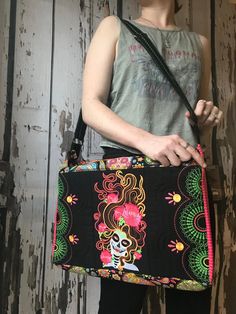 a woman holding a black purse with a colorful design on the front and side, standing in front of a wooden wall