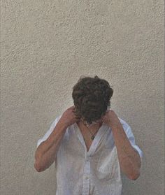 a woman covering her face with her hands while standing in front of a white wall