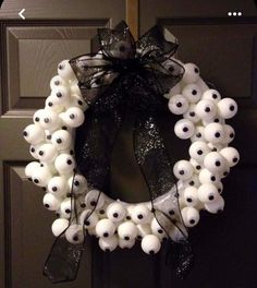 a wreath made out of white balls and black ribbon with eyes painted on the front door