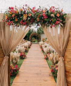 an outdoor ceremony with flowers on the aisle and draping over the doorways