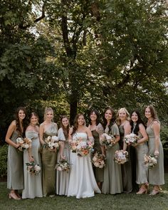 a group of women standing next to each other in front of trees and grass with bouquets