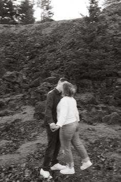 black and white photograph of two people embracing each other in front of some rocks on the side of a hill