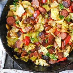 a skillet filled with sausage, cabbage and red peppers on top of a table