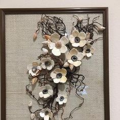 an art piece with white and black flowers in a brown frame on the side of a wall