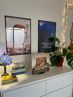 a white dresser topped with lots of books next to a wall covered in pictures and lights