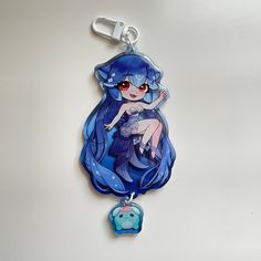 a keychain shaped like a cartoon character with blue hair and red eyes sitting on top of a white surface