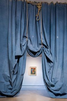 the curtains are open in an empty room with paintings on the wall behind them and hanging from ropes