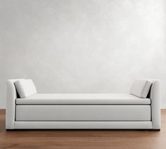 a white couch sitting on top of a hard wood floor next to a gray wall