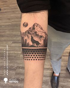 a man with a wolf tattoo on his arm and leg, standing in front of a mountain