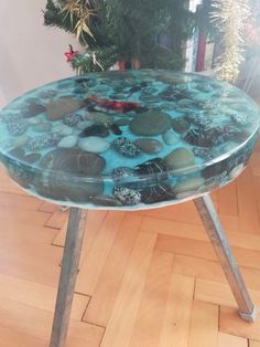 a glass table with rocks on it in the middle of a wooden floor next to a christmas tree