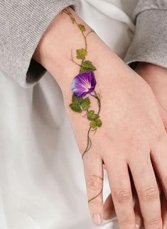 a woman's hand with a purple flower tattoo on her left wrist and green leaves