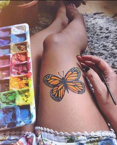 a woman with a butterfly tattoo on her arm next to some paintbrushes and watercolors