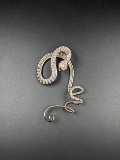 Intricate silver-plated woven wire and a manmade pink opal pearl create a twisting illusion of a snake clinging to your ear. A shimmering iridescent pale pink 'opal' resides in the head of this left side only ear cuff.  This serpent ear cuff has been polished to a bright silver shine and clear coated. The design for this ear cuff was inspired by a Lan Anh Handmade video. No piercings are required to enjoy wearing this ear cuff. The serpent's coils wrap around your outer ear using gentle tension and friction to hold the cuff in place. The cuff is around 2 1/4 inches in height and 1 3/8 inch in width. Silver Spiral Jewelry For Party, Elegant Silver Spiral Ear Cuff, Silver Wire Wrapped Ear Cuff For Party, Silver Snake-shaped Party Earrings, Party Silver Wire Wrapped Ear Cuff, Sterling Silver Snake-shaped Jewelry For Parties, Sterling Silver Snake Shape Jewelry For Party, Elegant Silver Snake-shaped Earrings, Elegant Silver Snake Earrings