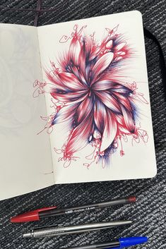 an open notebook with colored pencils and markers on the table next to it is a drawing of a flower