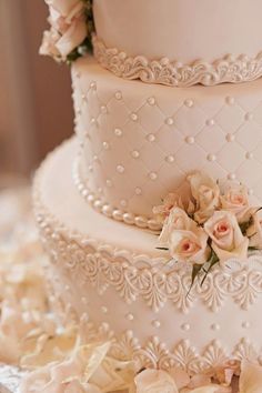 a three tiered white wedding cake with pink roses on the side and pearls around the edges