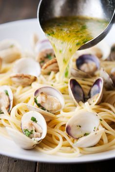 a plate of pasta with clams and sauce being drizzled over it