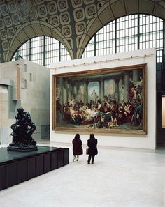 two people standing in front of a large painting inside of a building with arched windows