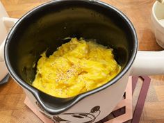 a pot filled with food sitting on top of a wooden table next to a cup