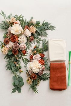 an arrangement of flowers and greenery laid out on a white surface next to a napkin