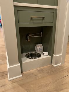 a kitchen sink in the corner of a room with wood floors and green cabinets on either side