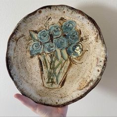 a hand holding a plate with blue flowers on it