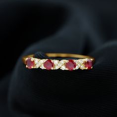 a gold ring with red and white stones on black fabric background, close up view