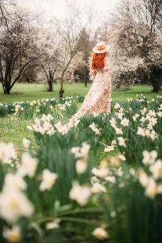 a woman standing in the middle of a field of flowers wearing a dress and hat