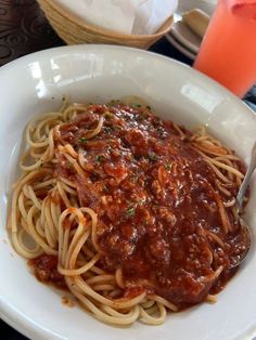 a white bowl filled with spaghetti and sauce on top of a table next to a glass of orange juice