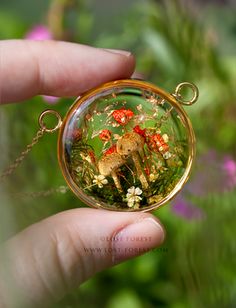 a hand holding a small glass pendant with a giraffe and flowers in it