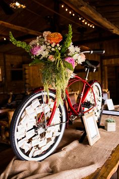 a red bicycle with flowers in the basket on it's front wheel sits on a table