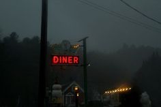 a diner sign lit up in the dark on a foggy day with no one around