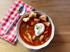 a bowl of soup with bread and sour cream on the side next to a red checkered napkin