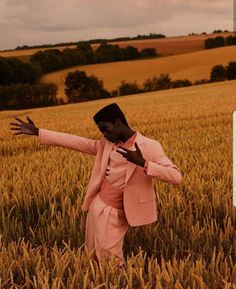 a man in a pink suit standing in a field with his arms out to the side