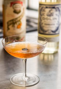 a close up of a drink in a wine glass on a table next to bottles