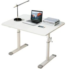 a laptop computer sitting on top of a white desk next to a lamp and book