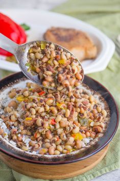 a spoon full of beans and rice in a bowl with some bread on the side