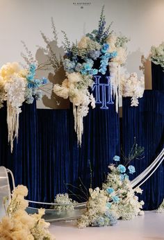 an arrangement of flowers on display in front of a blue curtained wall with white and light blue drapes