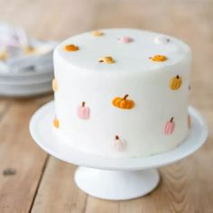 a white cake with pumpkins on it sitting on top of a wooden table next to plates