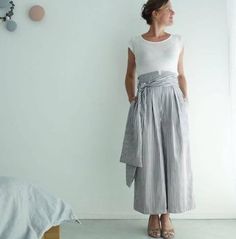 a woman standing in front of a wall wearing a white shirt and grey striped skirt