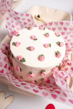 a white cake with pink frosting and roses on it sitting in a paper wrapper