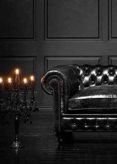 a black leather couch with candles on the floor in front of it and a wall behind it