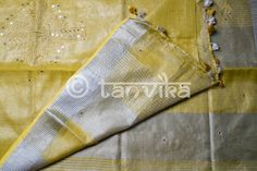 This elegant tissue linen drape in a beautiful gold tone features the beautiful and meticulously done floral cutwork design. This saree has pretty faux mirror (flattened sequin discs) work which adds a lovely vibe and bling to the whole outfit. The saree might have slight irregularities in the pattern & colors, which results from the human involvement in the process & is a hallmark of handcrafted products. Minor thread pulls are not considered damage. We recommend professional dry cleani Festive Linen Traditional Wear With Resham Embroidery, Traditional Gold Slub Silk Wear With Mirror Work, Festive Linen Traditional Wear With Zari Work, Festive Traditional Linen Wear With Zari Work, Gold Cotton Silk Saree With Gota Work, Celebration Tussar Silk Saree With Gota Work, Tussar Silk Saree With Gota Work For Celebrations, Festive Linen Traditional Wear For Weddings, Elegant Tussar Silk Dupatta With Mirror Work