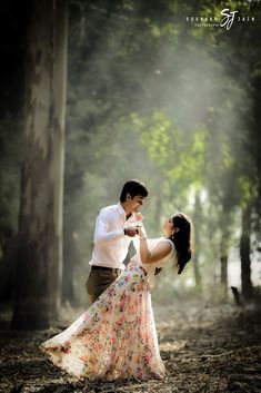 a man and woman dancing in the woods together with sunlight streaming through the trees behind them