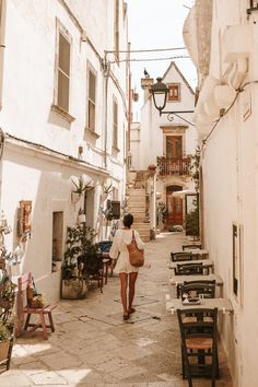 a woman walking down an alley way with tables and chairs on either side of her