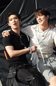 two young men sitting next to each other in front of a black sheet covered wall